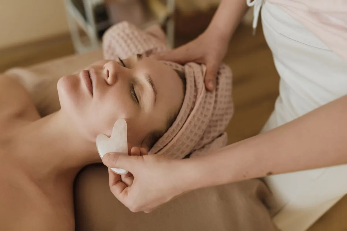 Therapist performing gua sha strokes along the cheekbone during a facial treatment